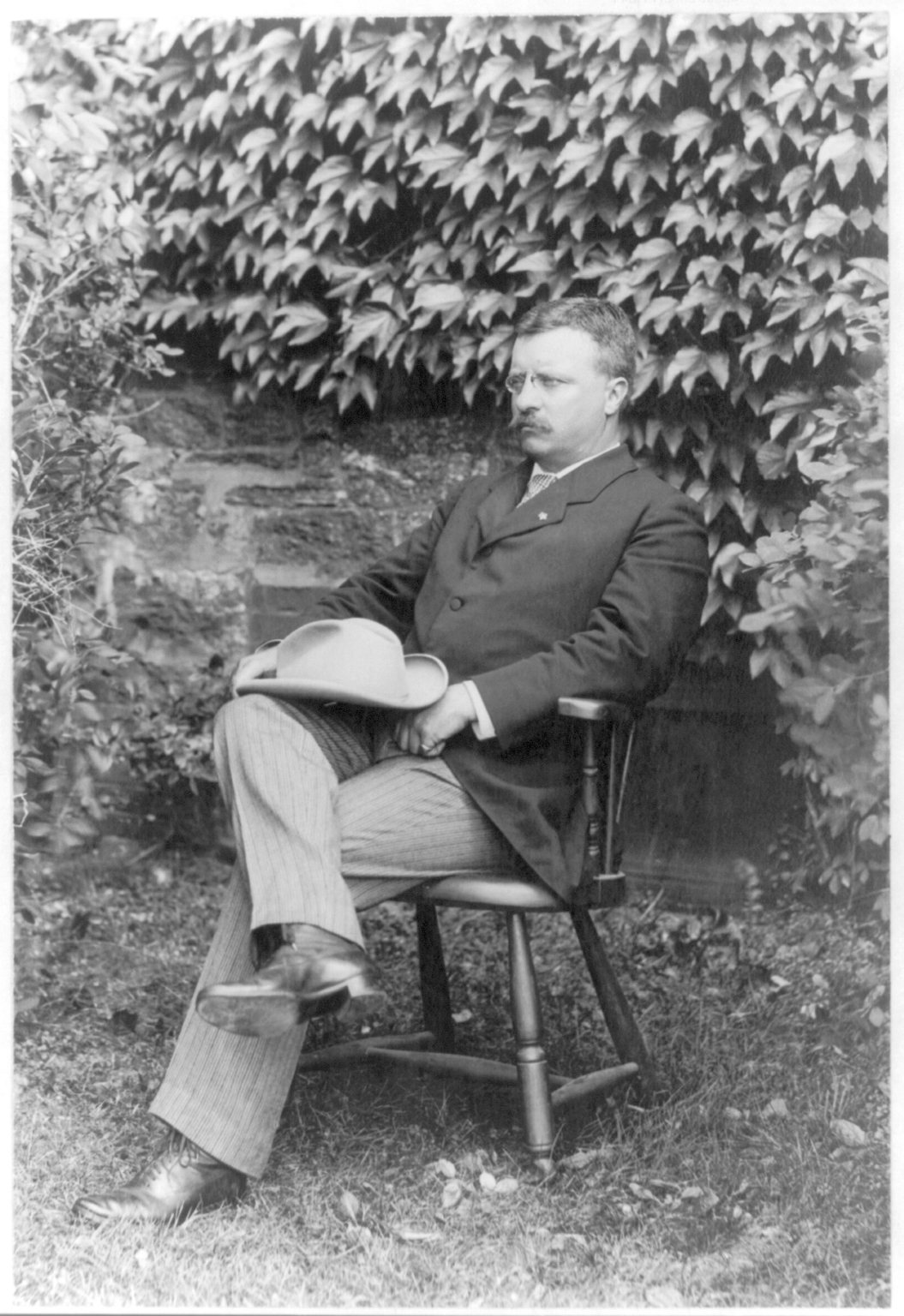 Photograph showing Theodore Roosevelt standing in an open area with lake behind him.